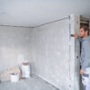 Worker using a Bosch 50m laser measure to calculate room dimensions on a construction site.